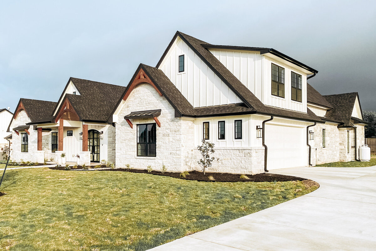 garage and front yard of limestone and white board and batten house with black windows