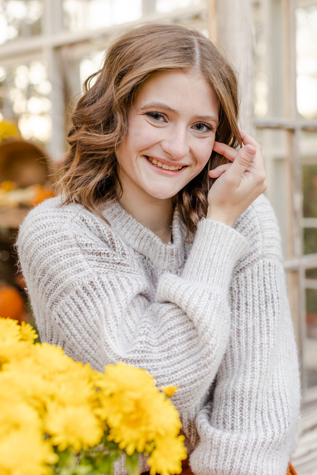 A Senior girl sits behind flowers and pushes hair out of face at a Senior Session in Lawrenceville