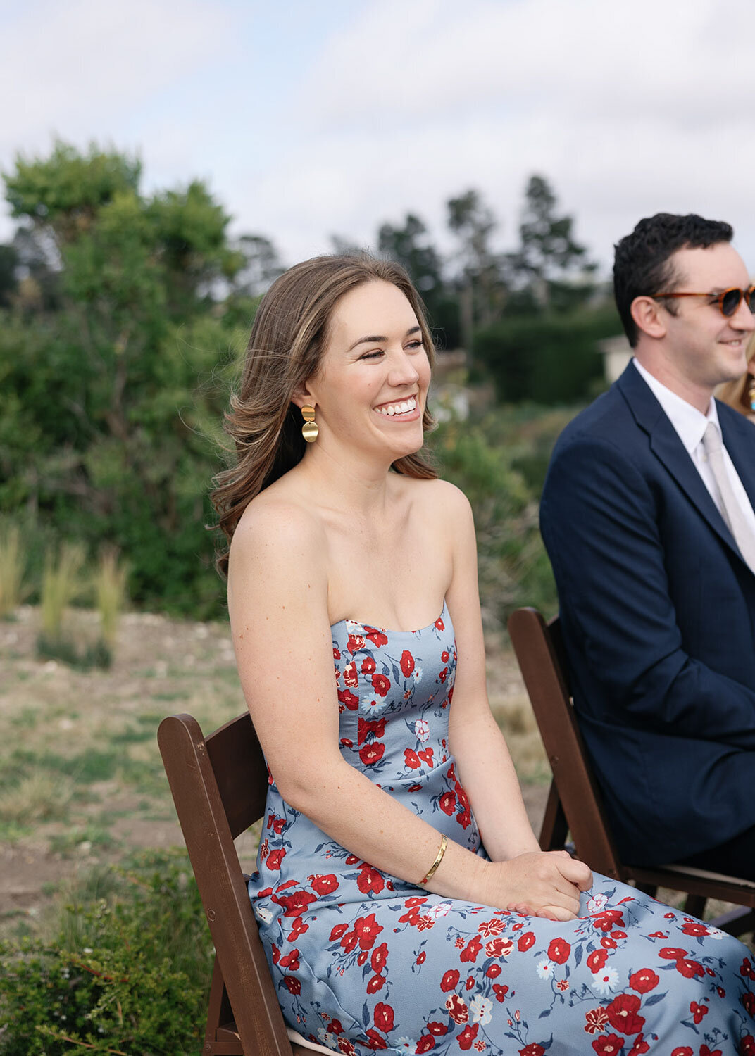 Guest in a floral blue dress smiling while seated at the ceremony