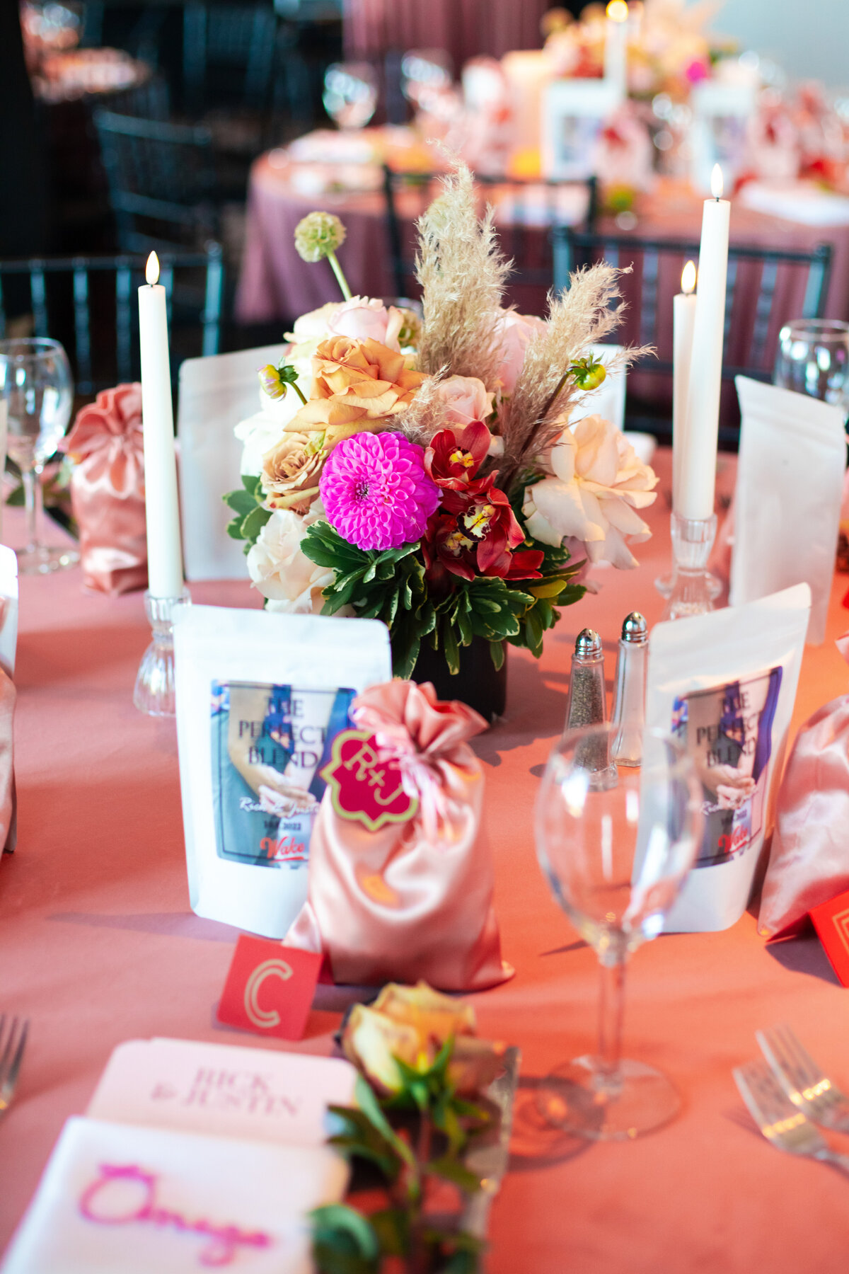 Table of colorful flowers, coffee and sweets favors, escort tags, candles, and menus at a wedding at The Terrace in Columbus, Ohio,