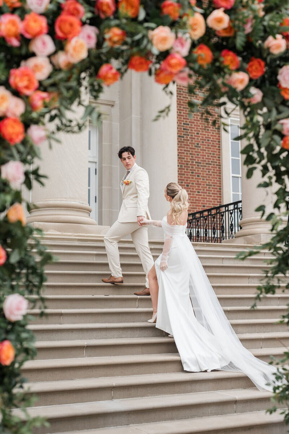 Bride and groom holding hands and walking up stairs, under a floral arch taken by wedding photographer in Cincinnati, OH