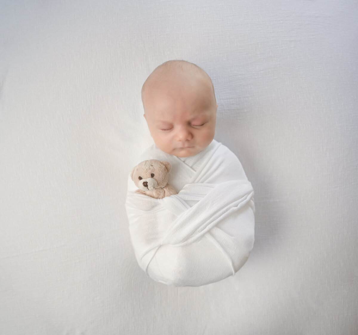 In home newborn photo session in Kitsap County, WA of a newborn wrapped in white and sleeping with a small teddy bear.