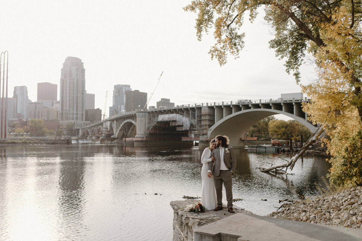 a bride and groom embracing with a lake and cityscape in the background