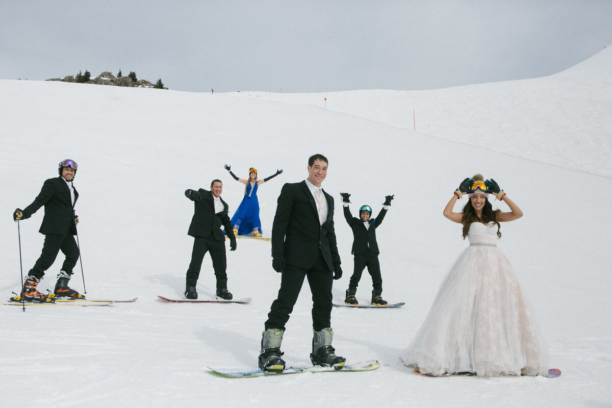 Bride, groom, and friends laughing in snow with snowboards and goggles – après-wedding energy in Kitzbühel by Studio Rose