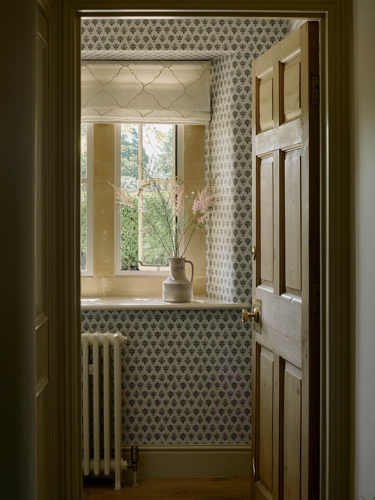 Look through into wallpapered bathroom with flowers in the window