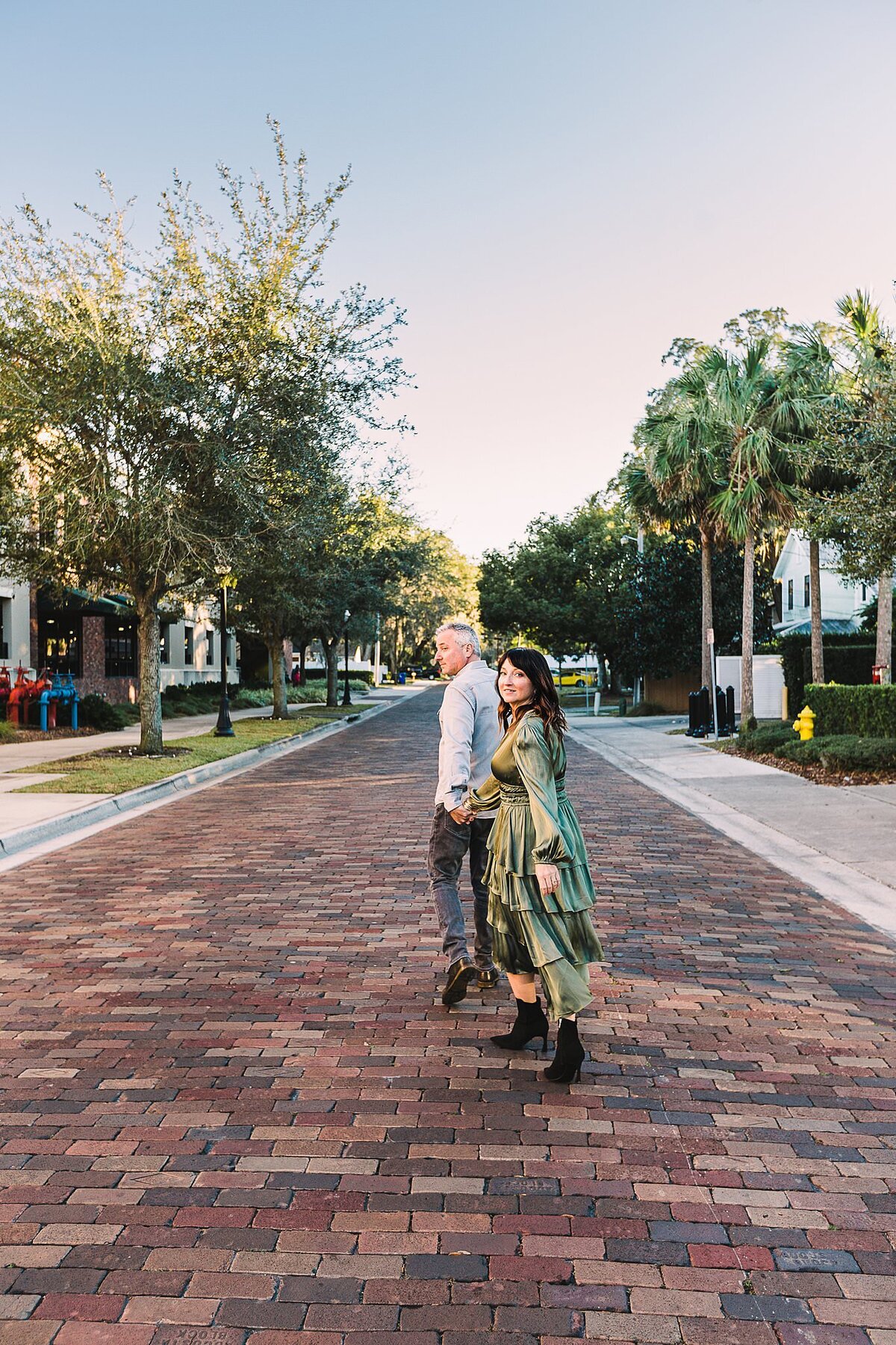 Couple holding hands walking on a cobblestone street holdind hands hans smiling, the man is leading the woman