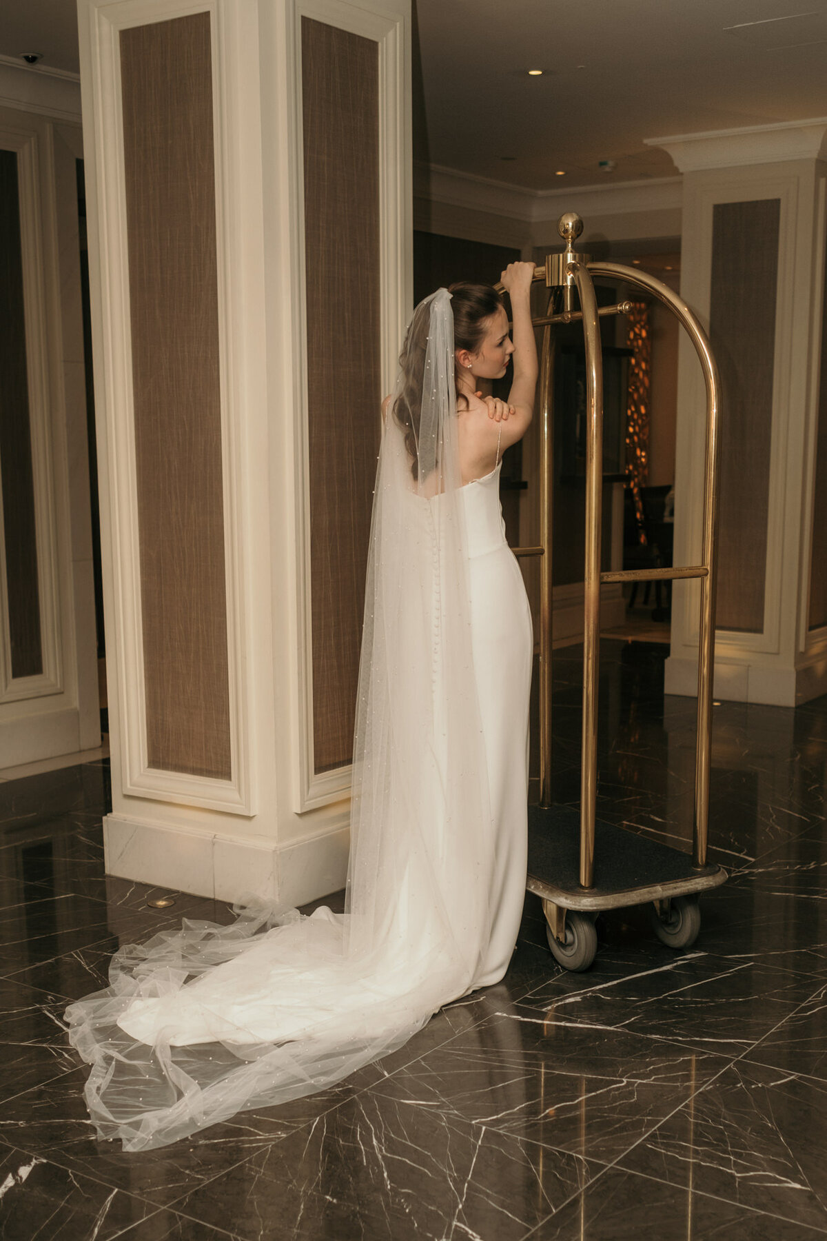 Mit dem Rücken zur Kamera hält sich das Brautmodel an einem hohen retro Kofferwagen fest.