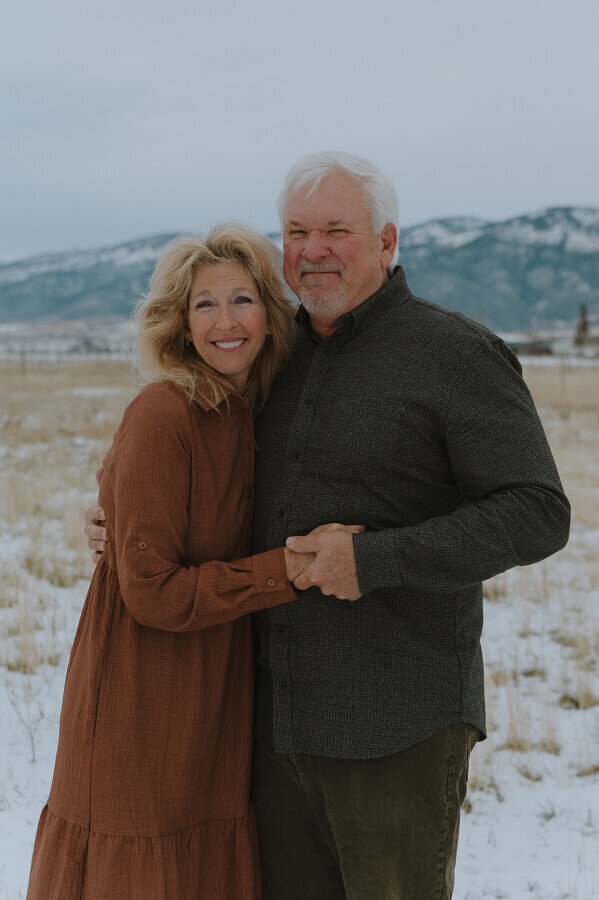 A husband and wife hold hands as the smile at the camera for a couples portrait during winter in Idaho Falls, ID.