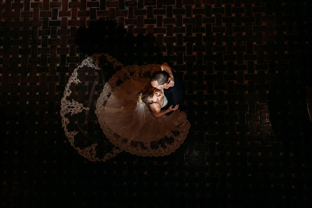 Groom kissing bride as she gazes up with joy in the lobby of Treasury on the Plaza, a dramatic and editorial wedding photo.