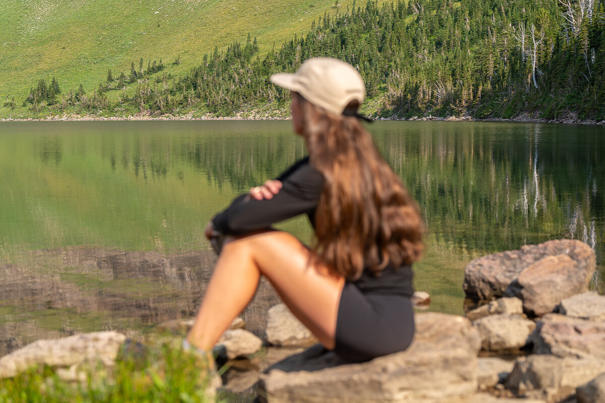 An image of a blurred woman with long brown hair who is sitting at the foot of Old Man Lake in Glacier National Park in Montana.