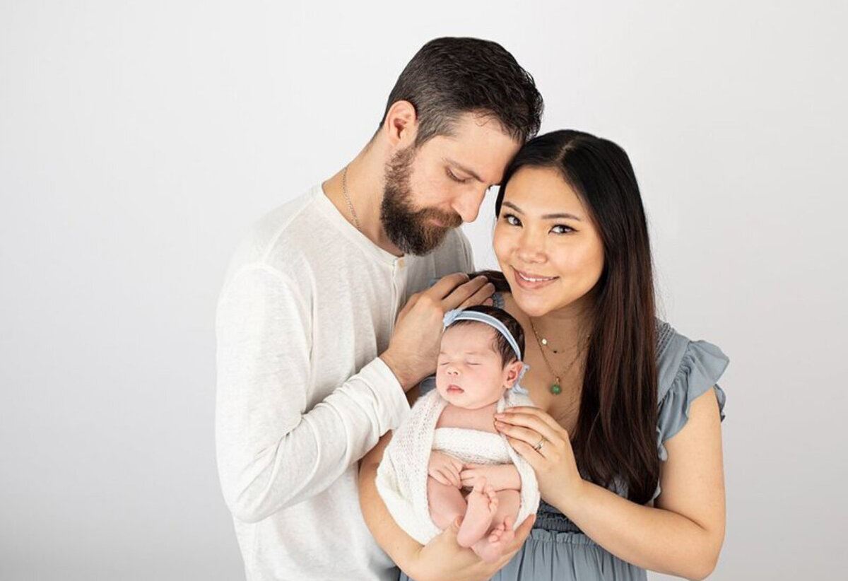Mom and dad with newborn baby girl cradled in mom's arms and father gently resting his forehead against the mother's head.