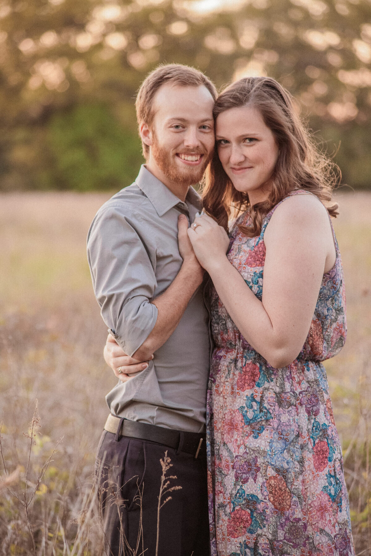 A couple in a sunlit field embrace each other and smile at the camera