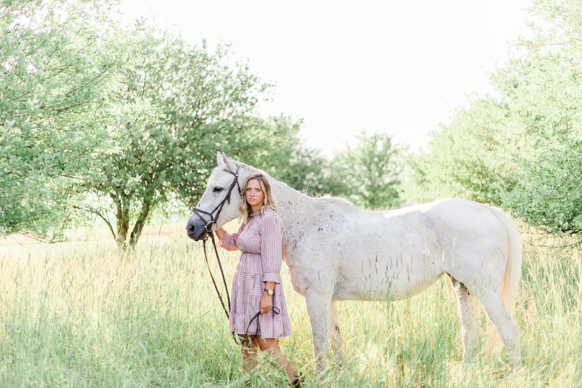 girl looking serious with a white horse in a field