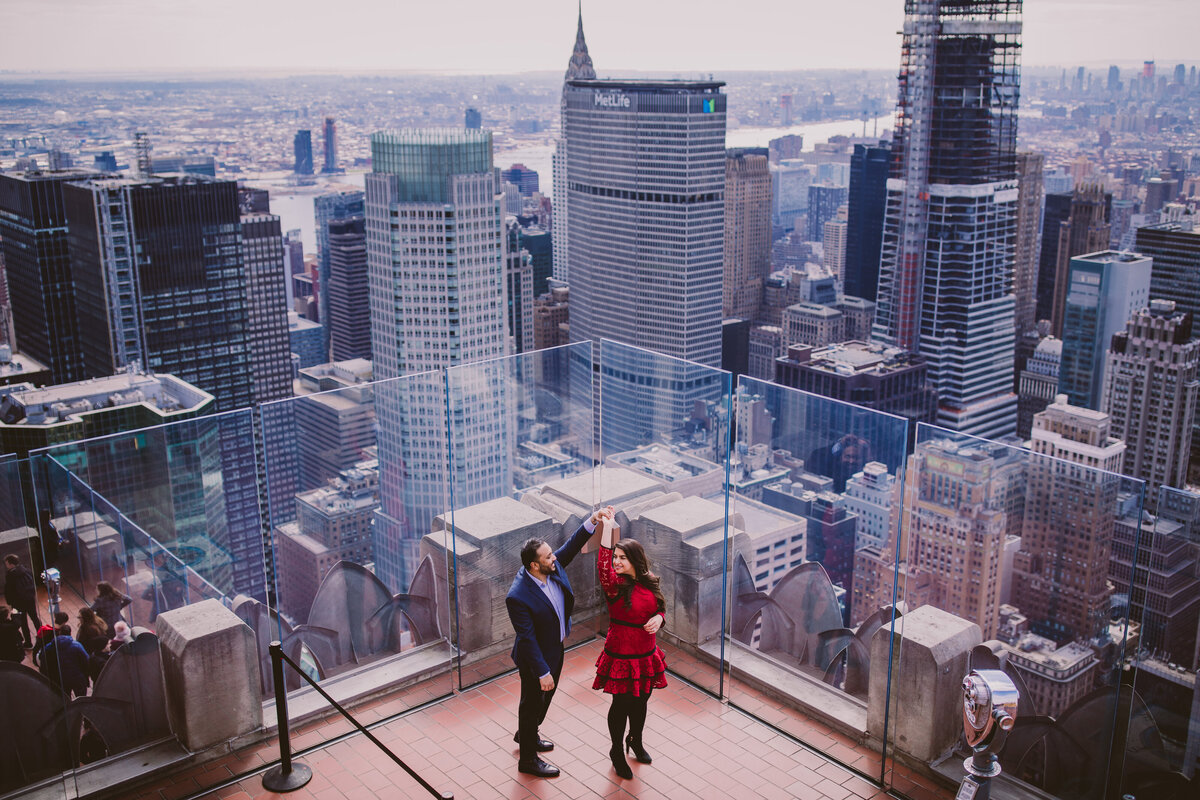 Groom twirling the bride during their engagement session at the viewing deck at the top of the rock in nyc