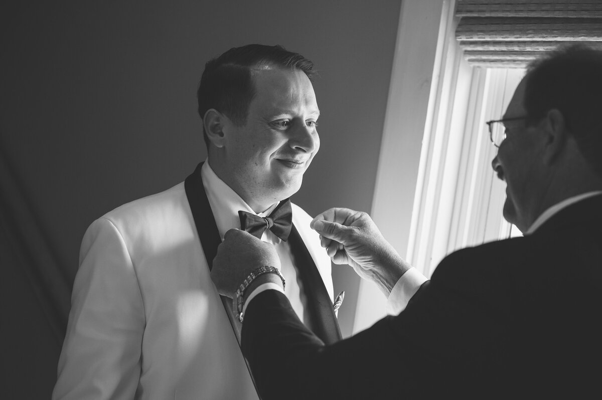 Father of groom fixing tuxedo tie.