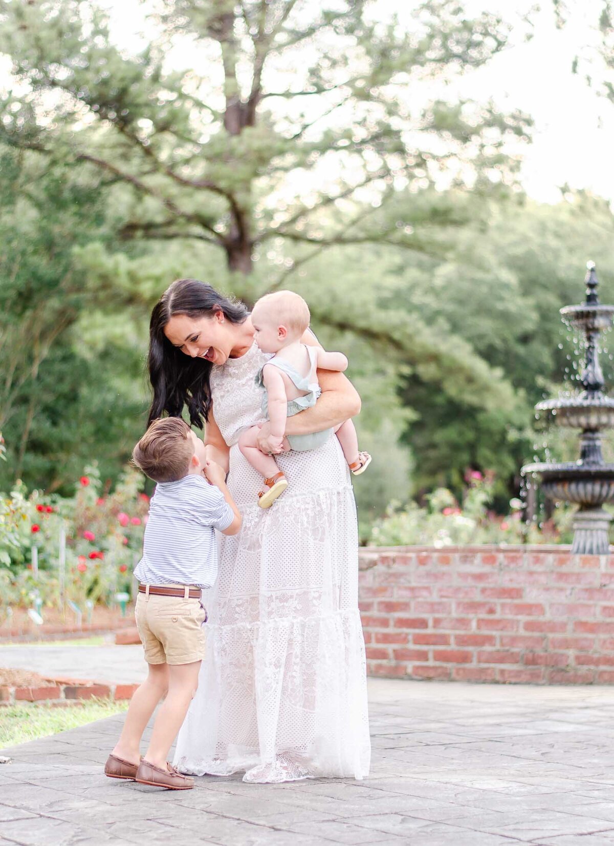 boy mom holds baby on her hip and smiles down at older son