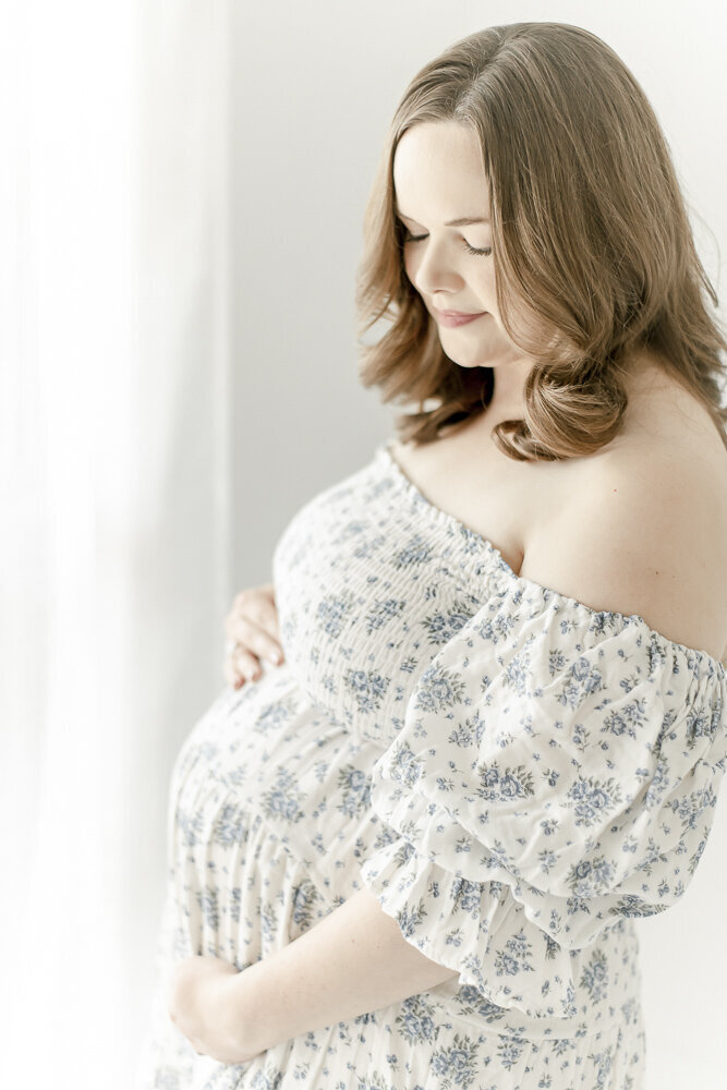 Pregnant woman in a blue floral dress looks at her stomach