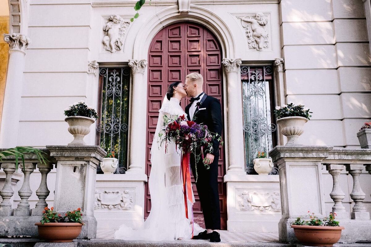 The bride and groom is kissing while standing on a vintage villa background