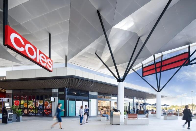 Exterior view of Carmel Village Shopping Centre featuring a modern Coles entrance with sleek architectural steel beams and signage. 