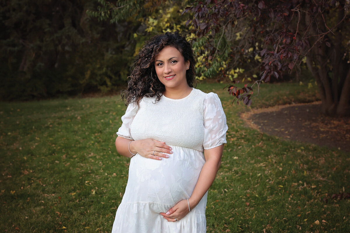 Pregnant mama in white dress in Confederation Park Calgary during photo shoot by Yuliia Terziian Photography.