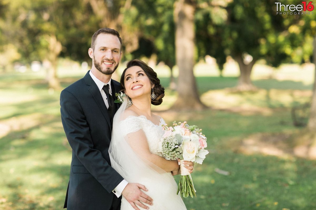 Bride looks back at her Groom with a smile as he embraces her from behind