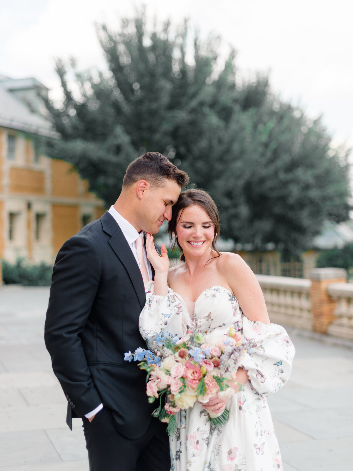 Bride and groom share an intimate moment on the terrace of Cairnwood Estate, captured by Philadelphia Fine Art Wedding Photographer Elizabeth Kane. The bride’s romantic floral gown and pastel bouquet echo the editorial elegance and timeless charm of this iconic Pennsylvania wedding venue.
