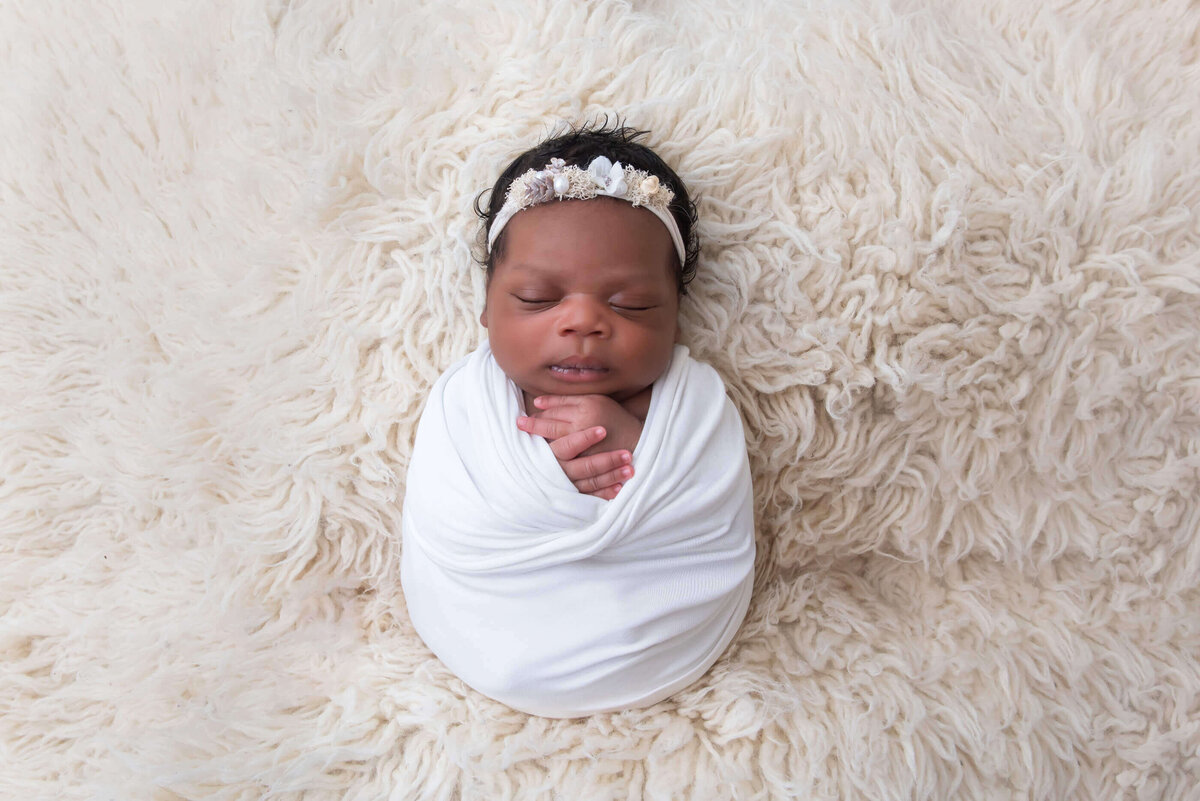 black newborn baby girl wrapped in white on a cream coloured rug for her newborn photography session