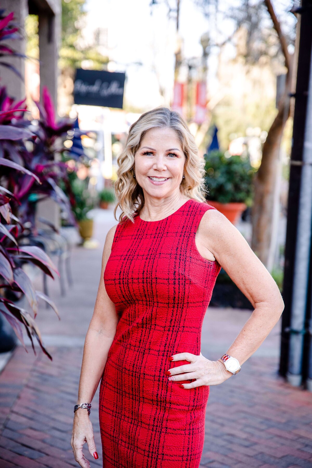 Business headshot of women in a red dress with one hand on her hip smiling while standing on a brick sidewalk downtown for a brand photo shoot with commercial photographers