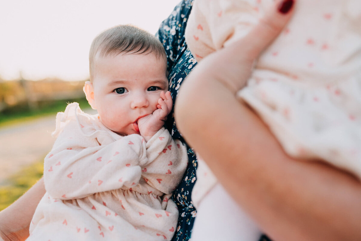 A baby girl sucks her thumb while her mother holds bother her and her twin sister