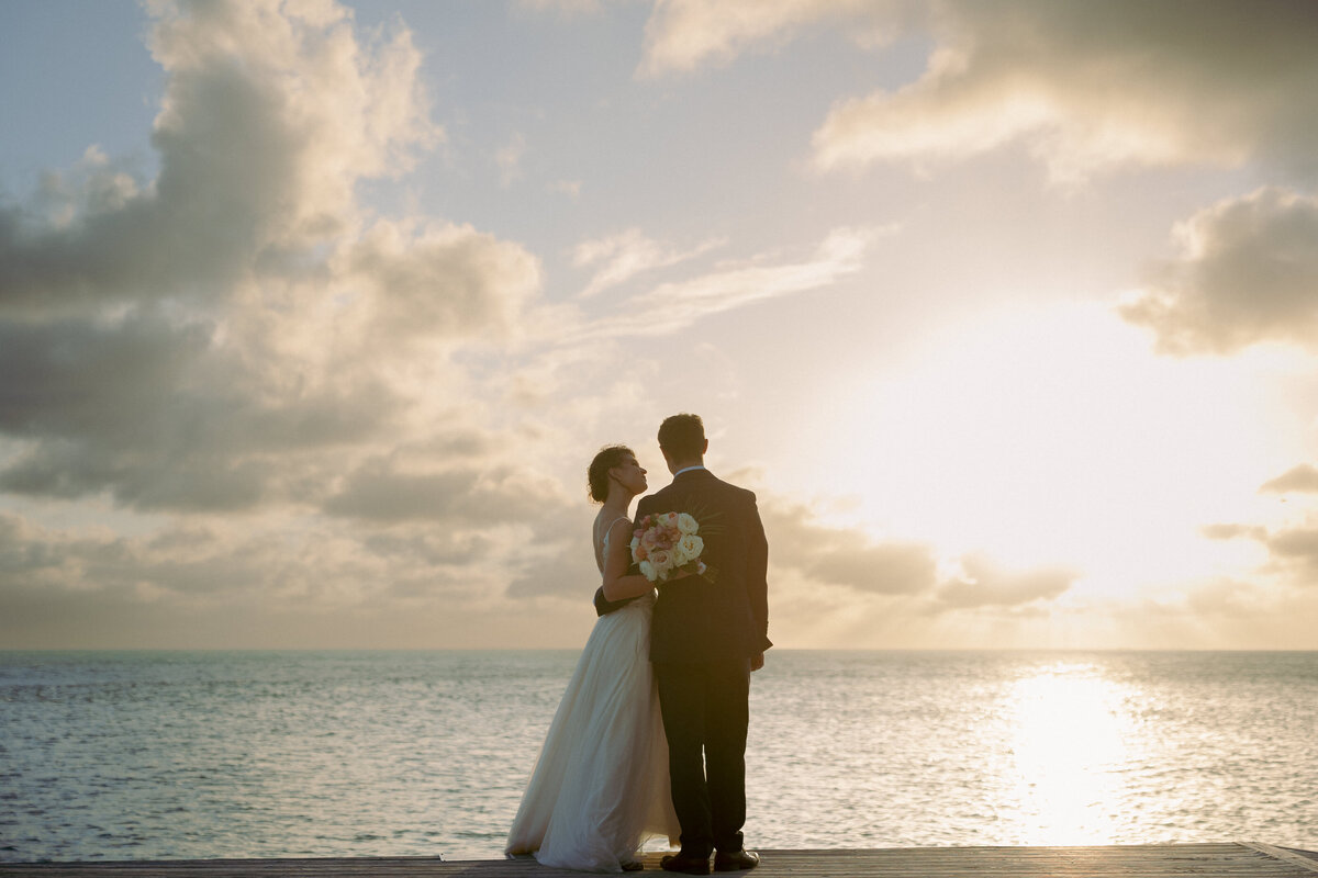 bride and groom standing on the beach at sunset in front of the ocean