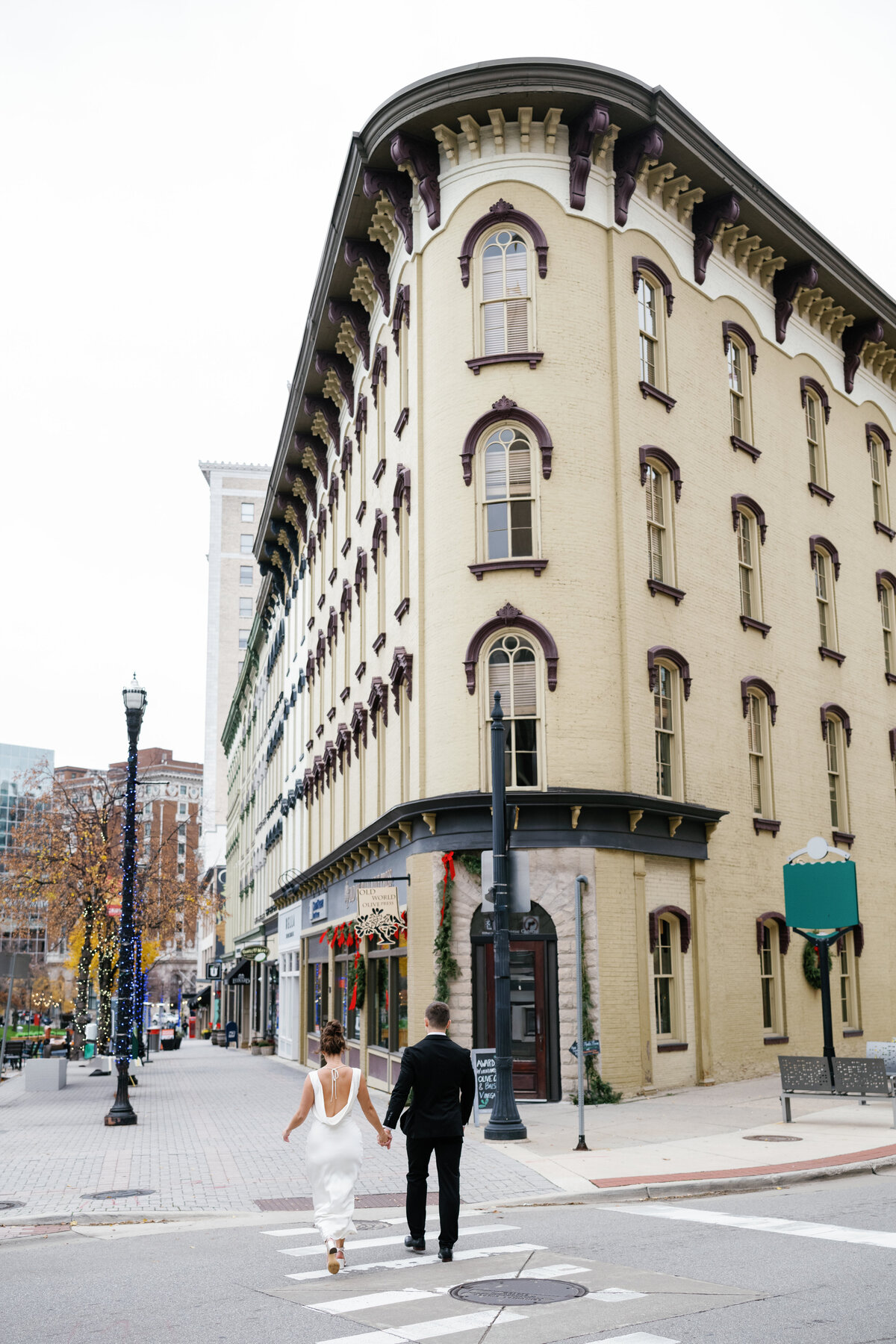 a bride and groom walk across the street in downtown Grand Rapids holding hands