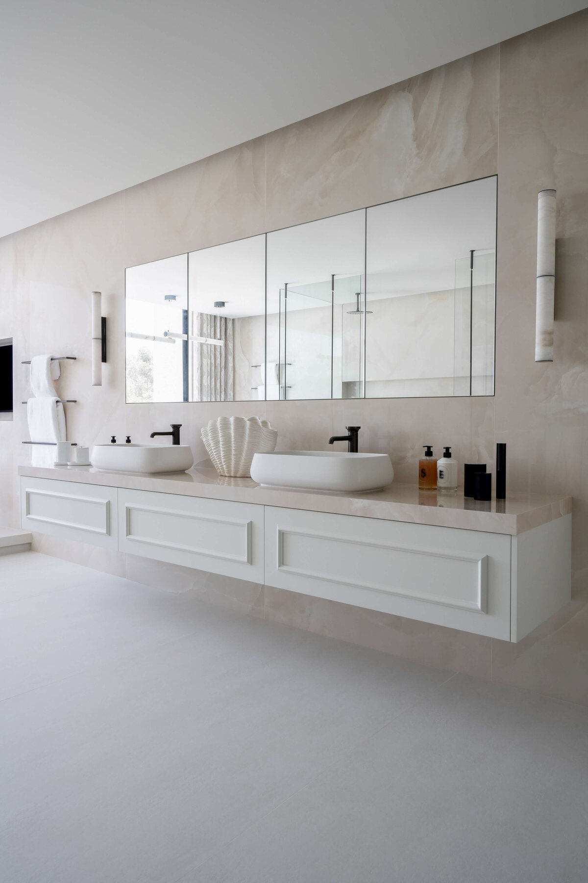 Large double-sink in a primary bathroom, with a focus on light, neutral tones. The sinks are white on a light marble counter, with a large mirror above them.