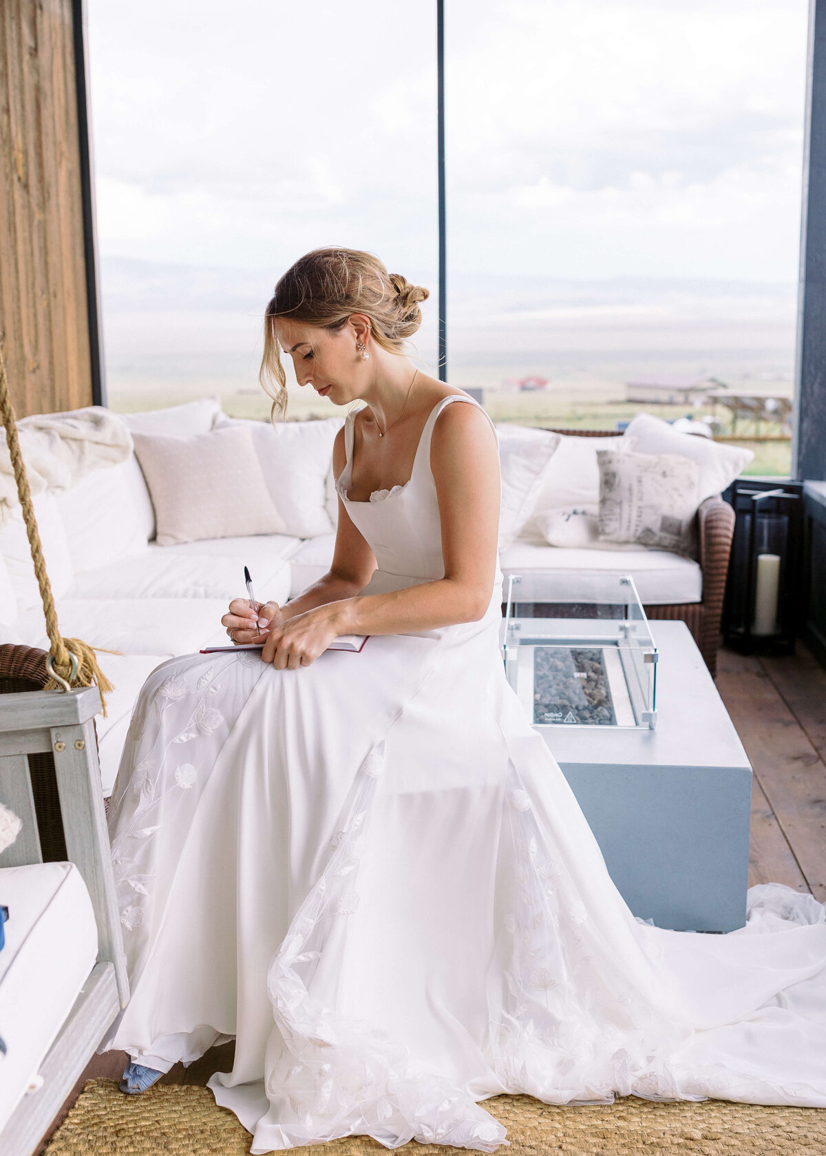 The bride sits on the porch of a cabin while she finishes writing down her vows
