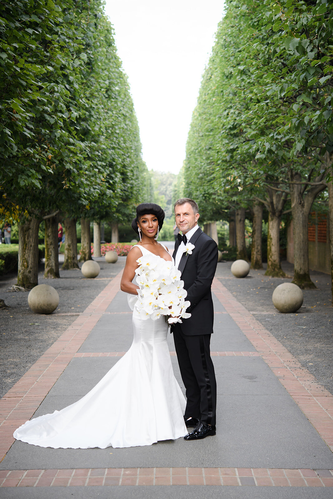 bride and groom elegantly dressed, surrounded by a green tree-lined aisle, and the second shows a beautifully decorated aisle with white orchids and hydrangeas, embodying the essence of a sophisticated garden wedding.