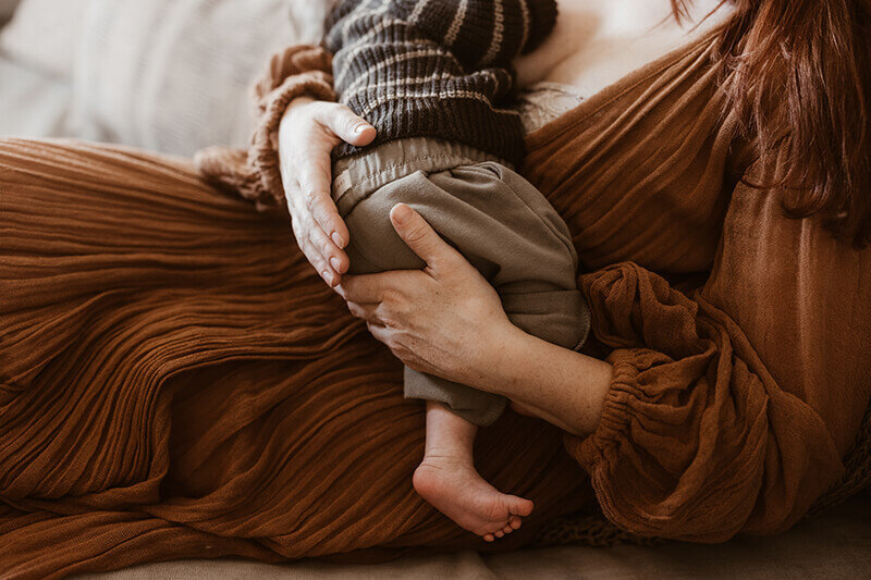 Close up of mom holding newborn baby boy and his feet dangling near her hip