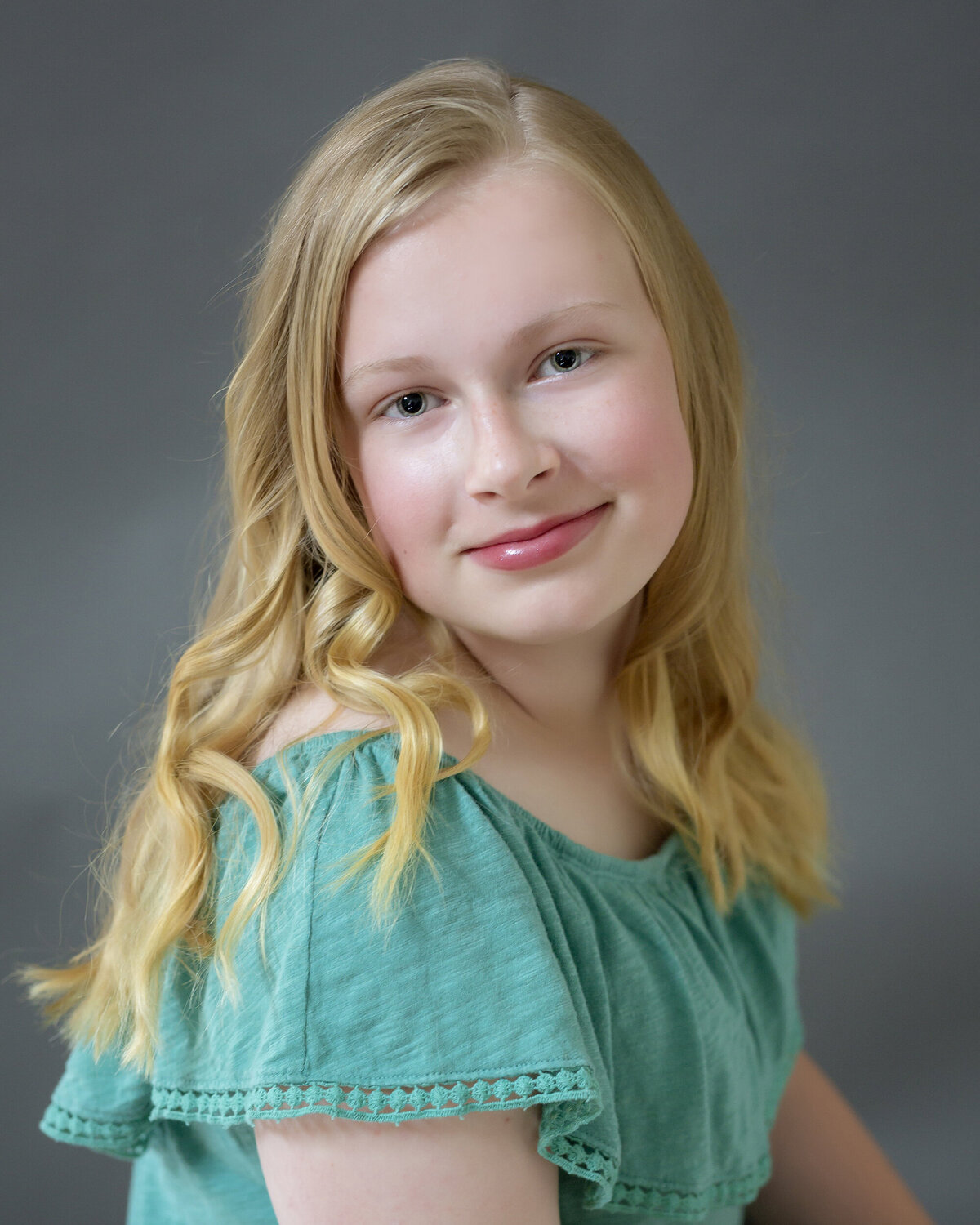 Female child actor headshot  wearing a light green blouse & smiling at the camera