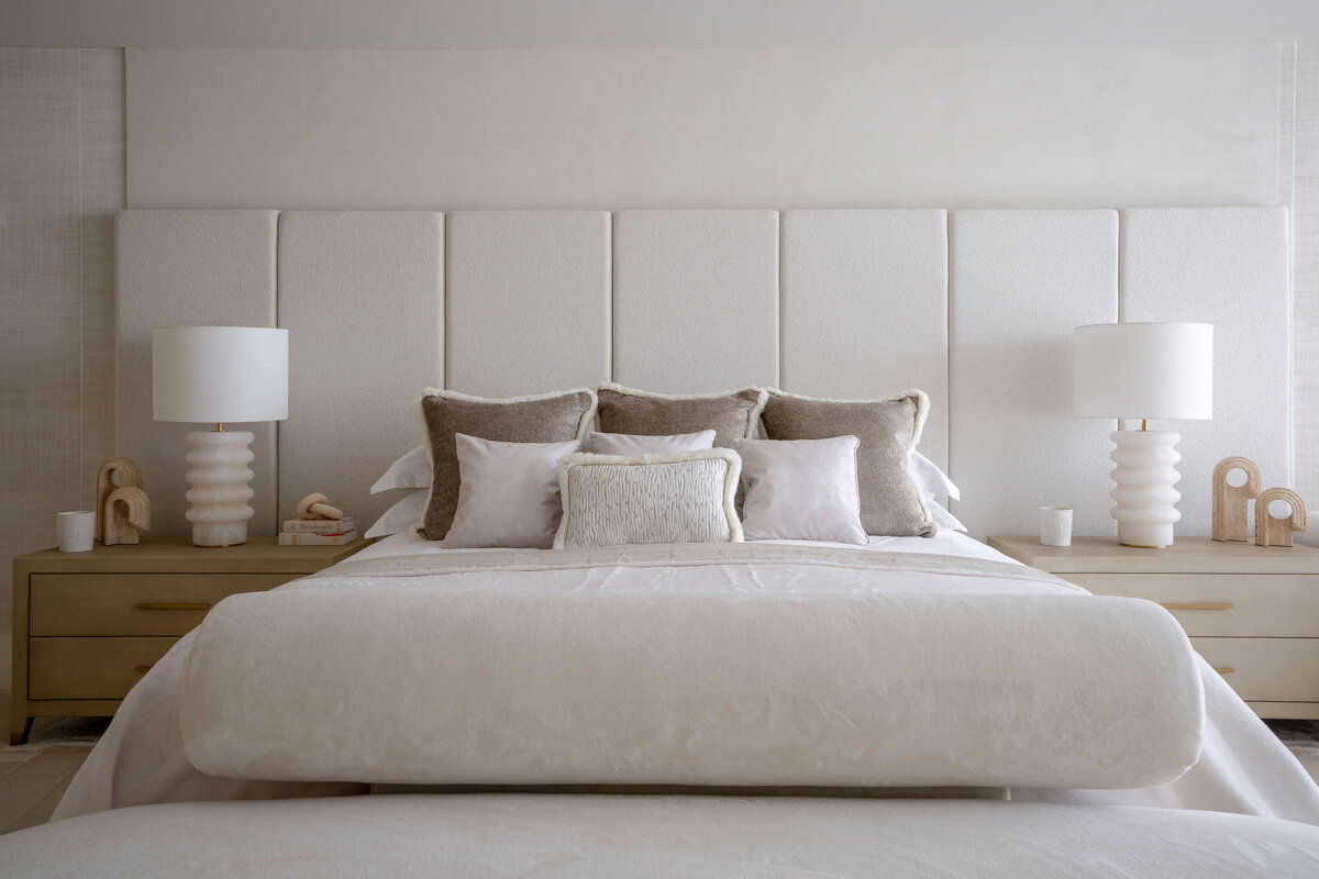 The soft white bedding on the primary bed is accented with neutral throw pillows, and two light bedside tables adorned with white lamps.