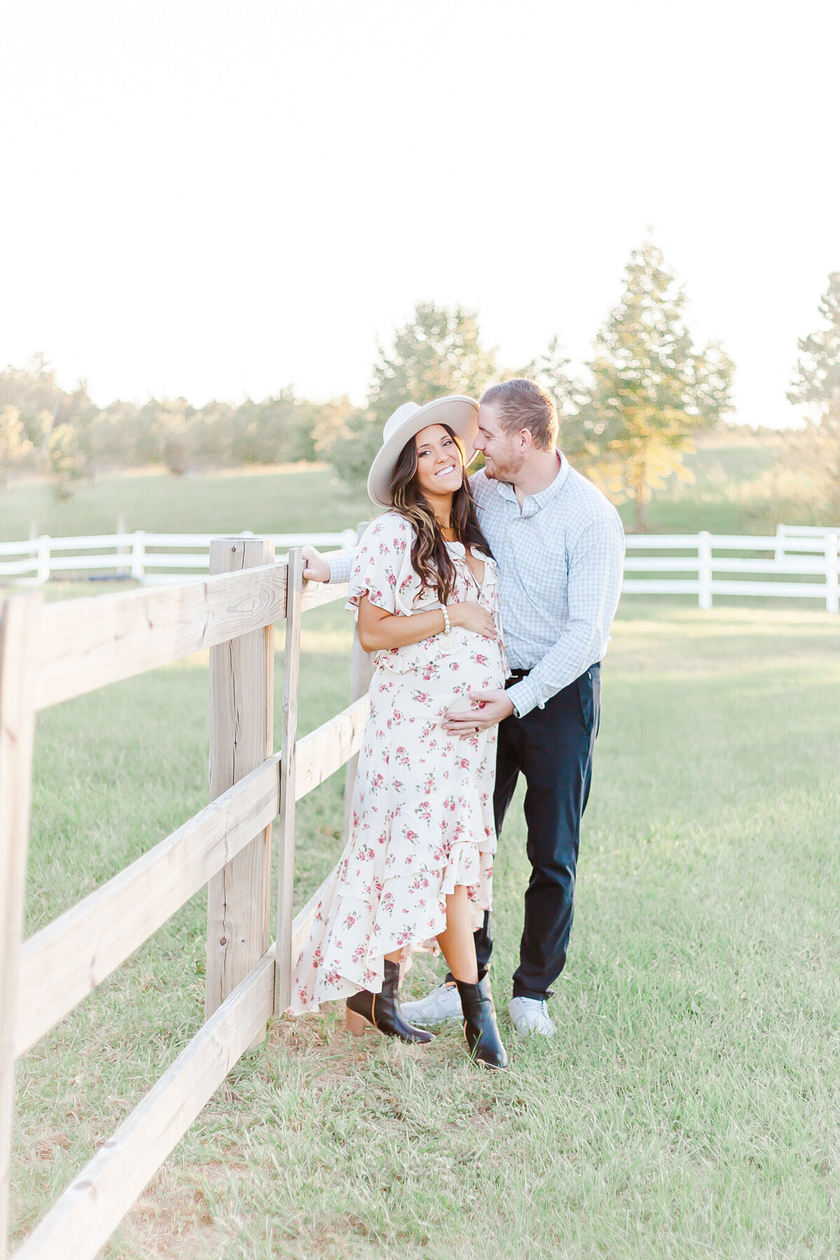 Mom smiling at camera while dad is smiling at mom and holding pregnant belly during maternity session