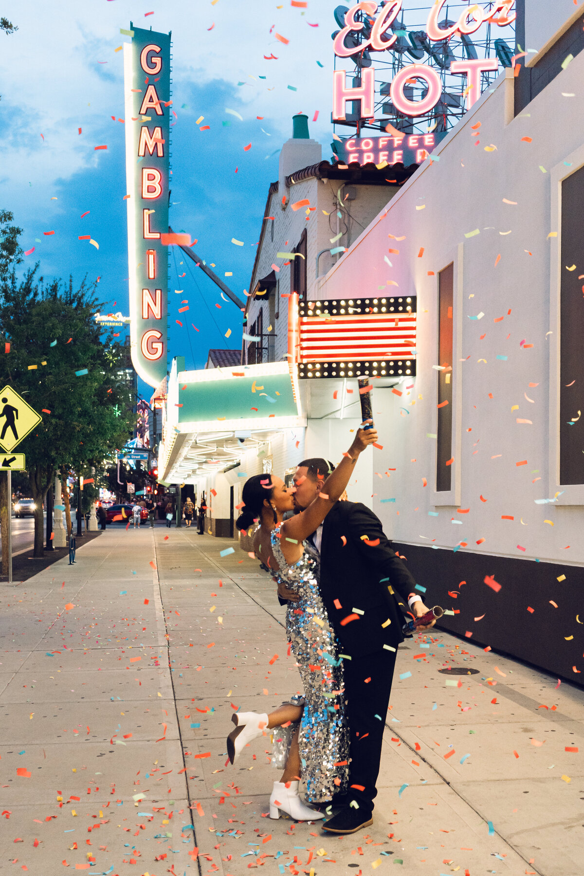 Engaged couple in Vegas at twilight kissing each other as confetti streams down under neon lights