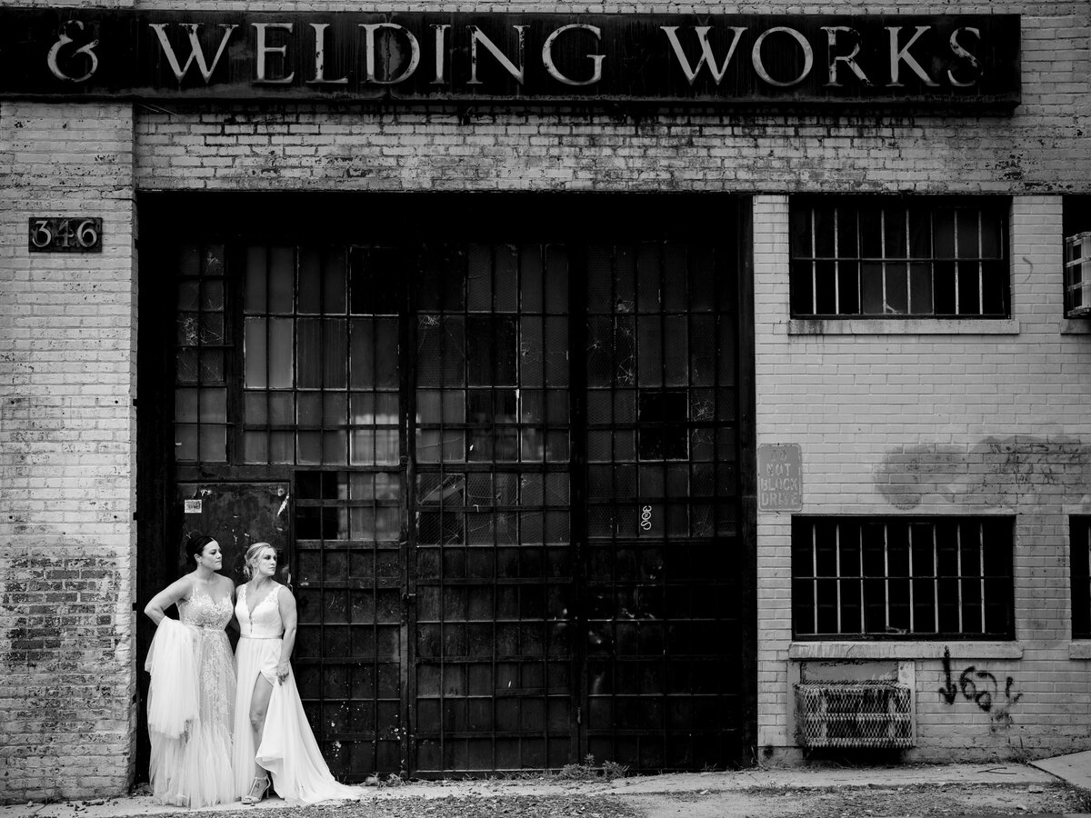 Two brides standing together against an industrial style building