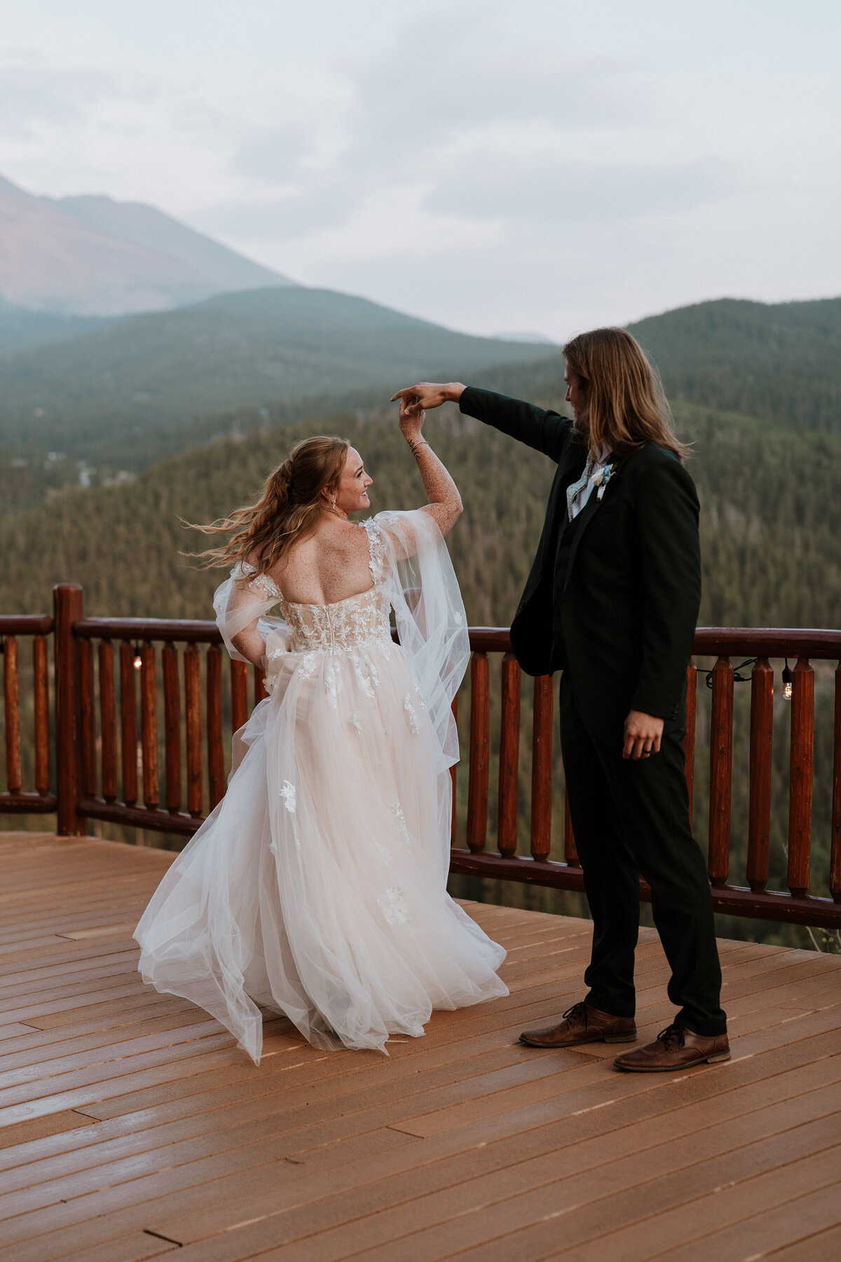Bride twirls joyfully with groom on wooden deck of the Lodge at Breckenridge surrounded by mountain views.