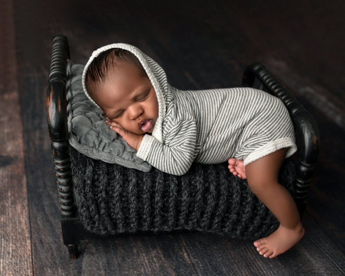 Sleeping baby boy in striped outfit posed on mini black bed – Liberty Hill and North Austin newborn photographer