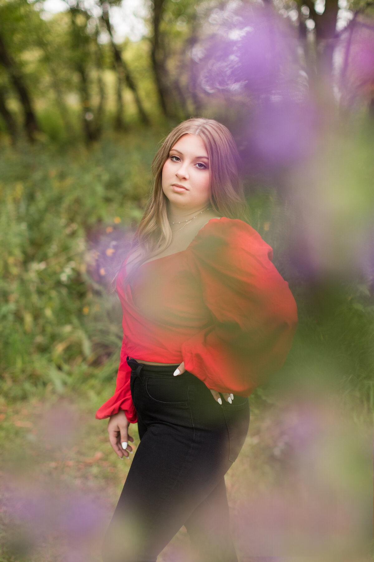 Senior girl standing behind a purple flower bush looking at the camera