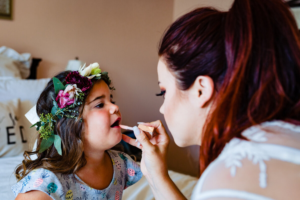 One of the top wedding photos of 2020. Taken by Adore Wedding Photography- Toledo, Ohio Wedding Photographers. This photo is of a bride putting lipstick on the flower girl before the wedding ceremony
