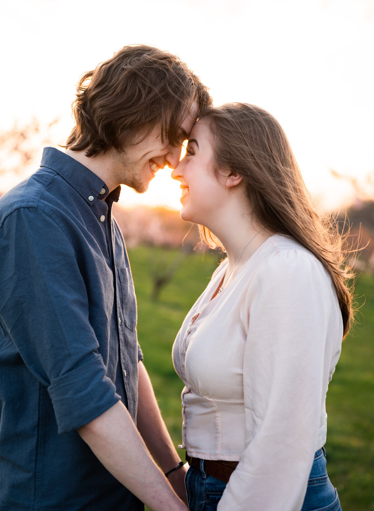 A romantic outdoor photo of a couple sharing a joyful moment, smiling and forehead-to-forehead during golden hour