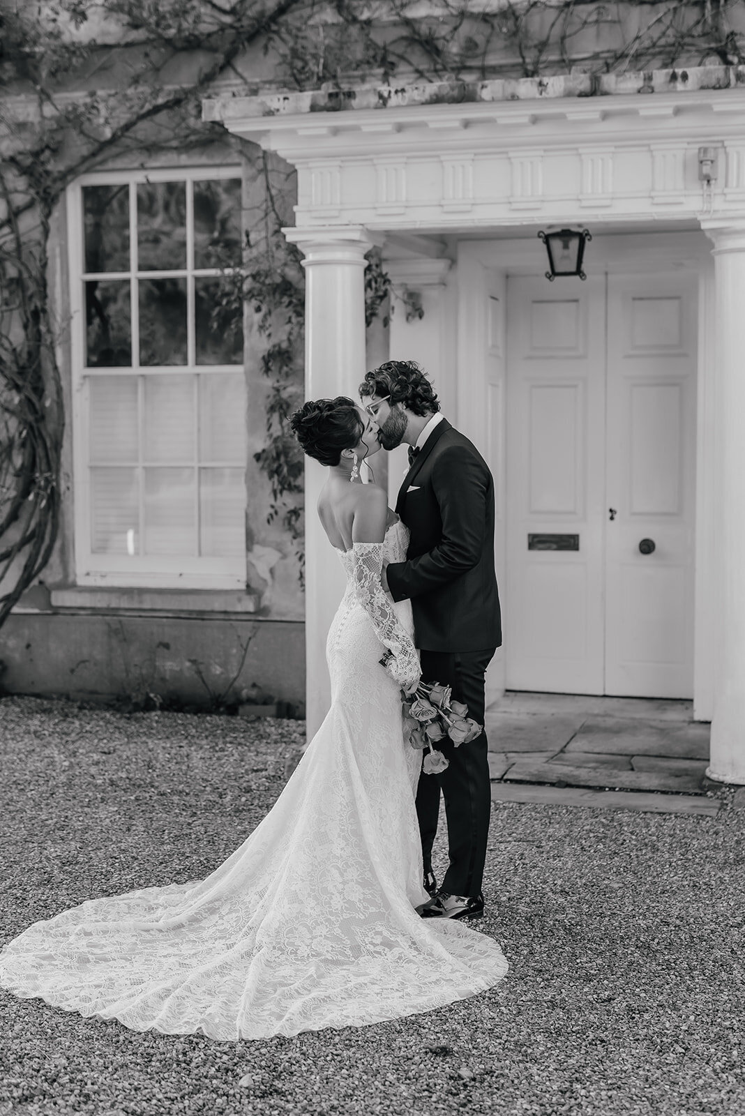 Bride and Groom kissing in front of white pillar doorway at Northbrook Park, Farnham