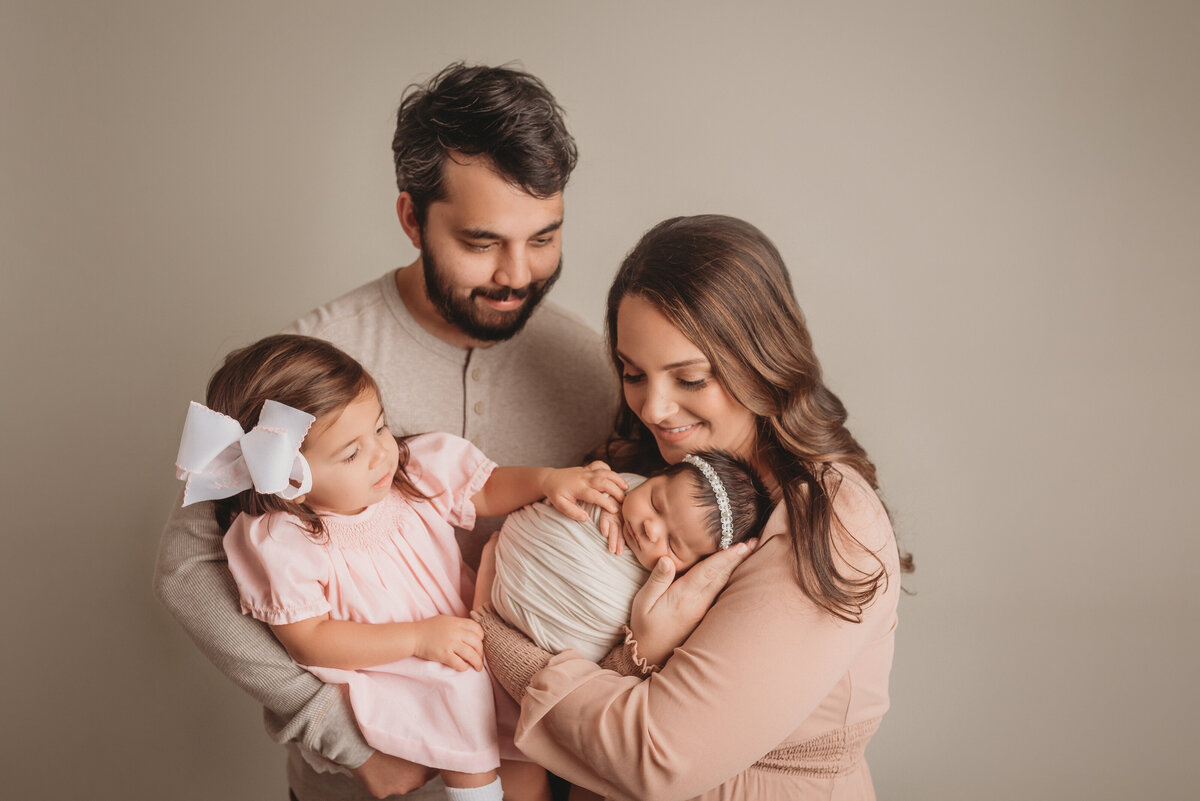 Family of 4 posing at Atlanta newborn photography studio looking at newborn baby girl while mom holds her