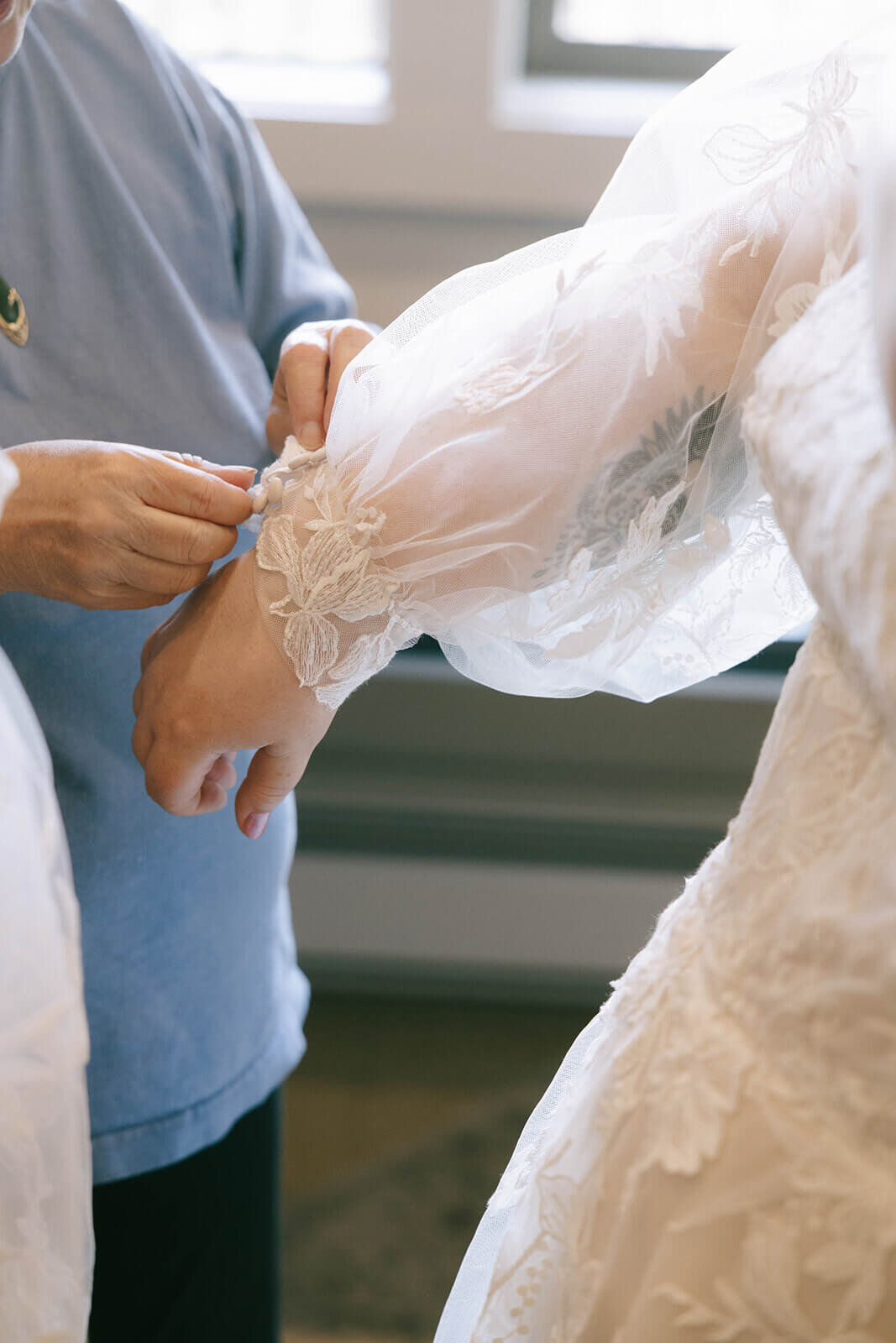 A bride getting the sleeve of her wedding dress buttoned.