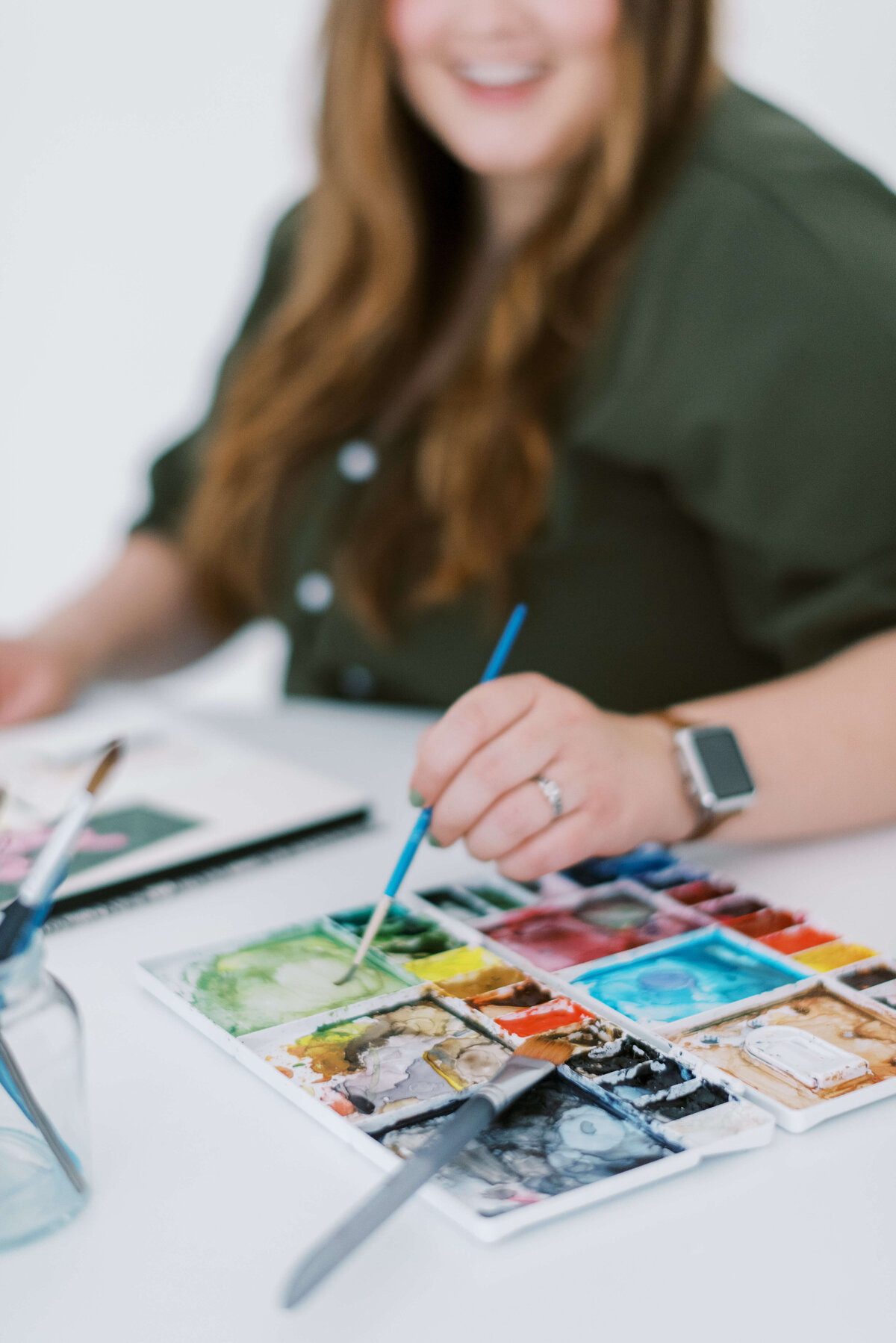 Elyse of E Stokes Creations using a watercolor brush and dipping into her paint palette of watercolor.