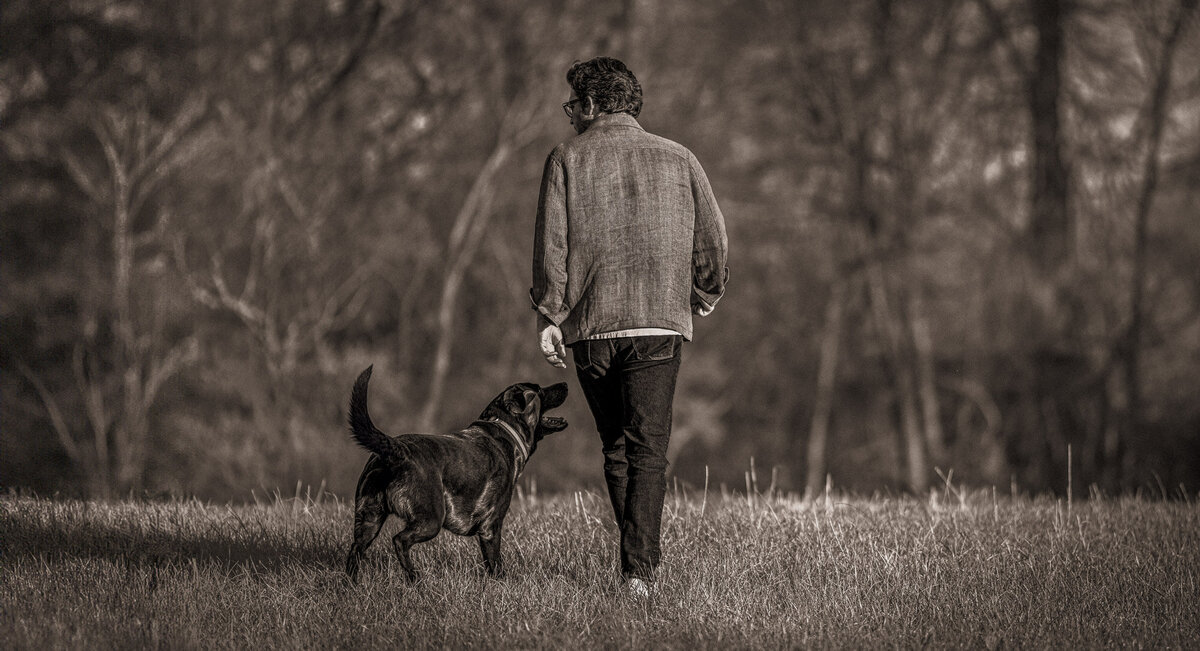 a chocolate lab and his human man walking away from the camera in black and white in the woods